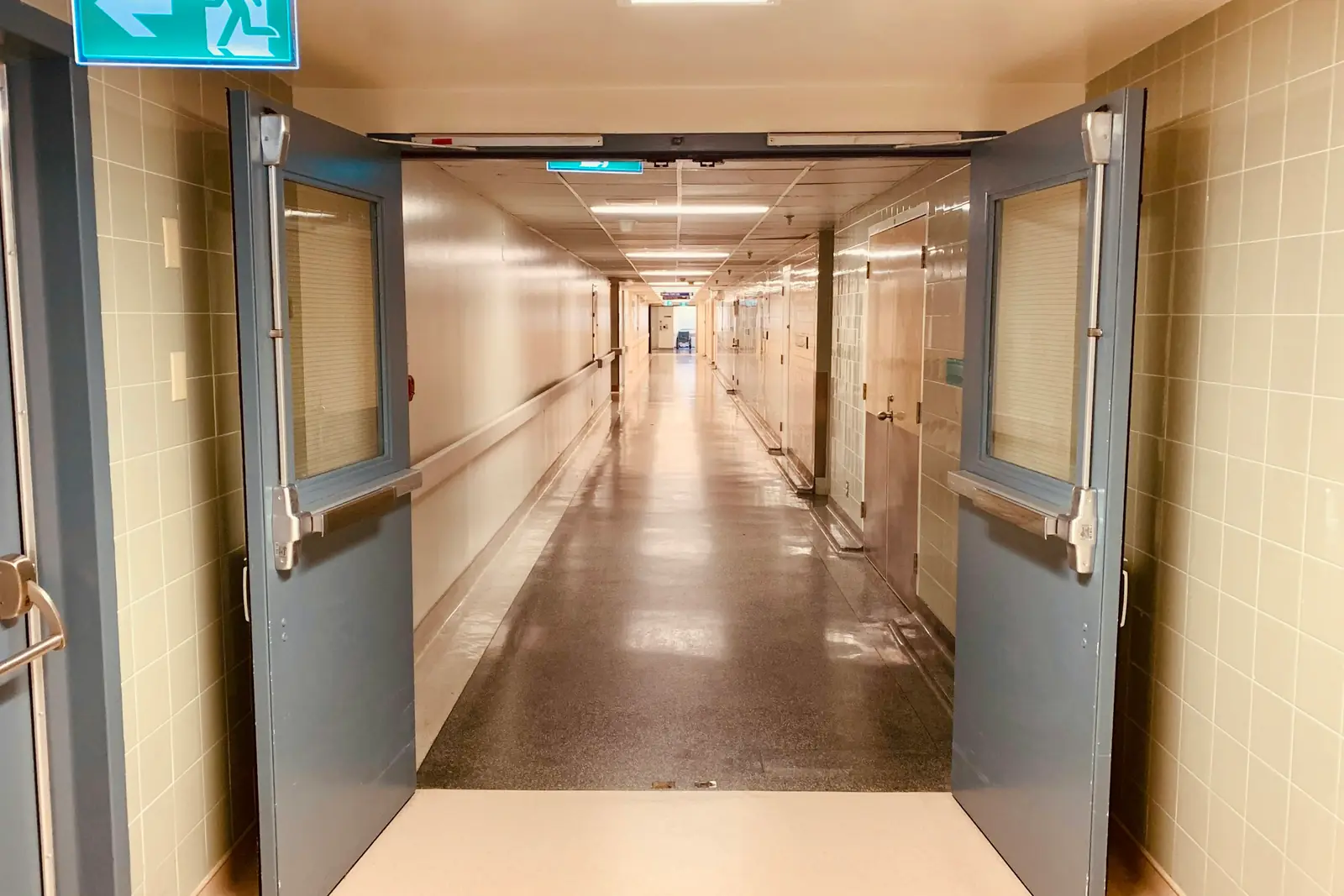 Openstaande klapdeuren naar een lange, lege ziekenhuisgang met glanzende vloer